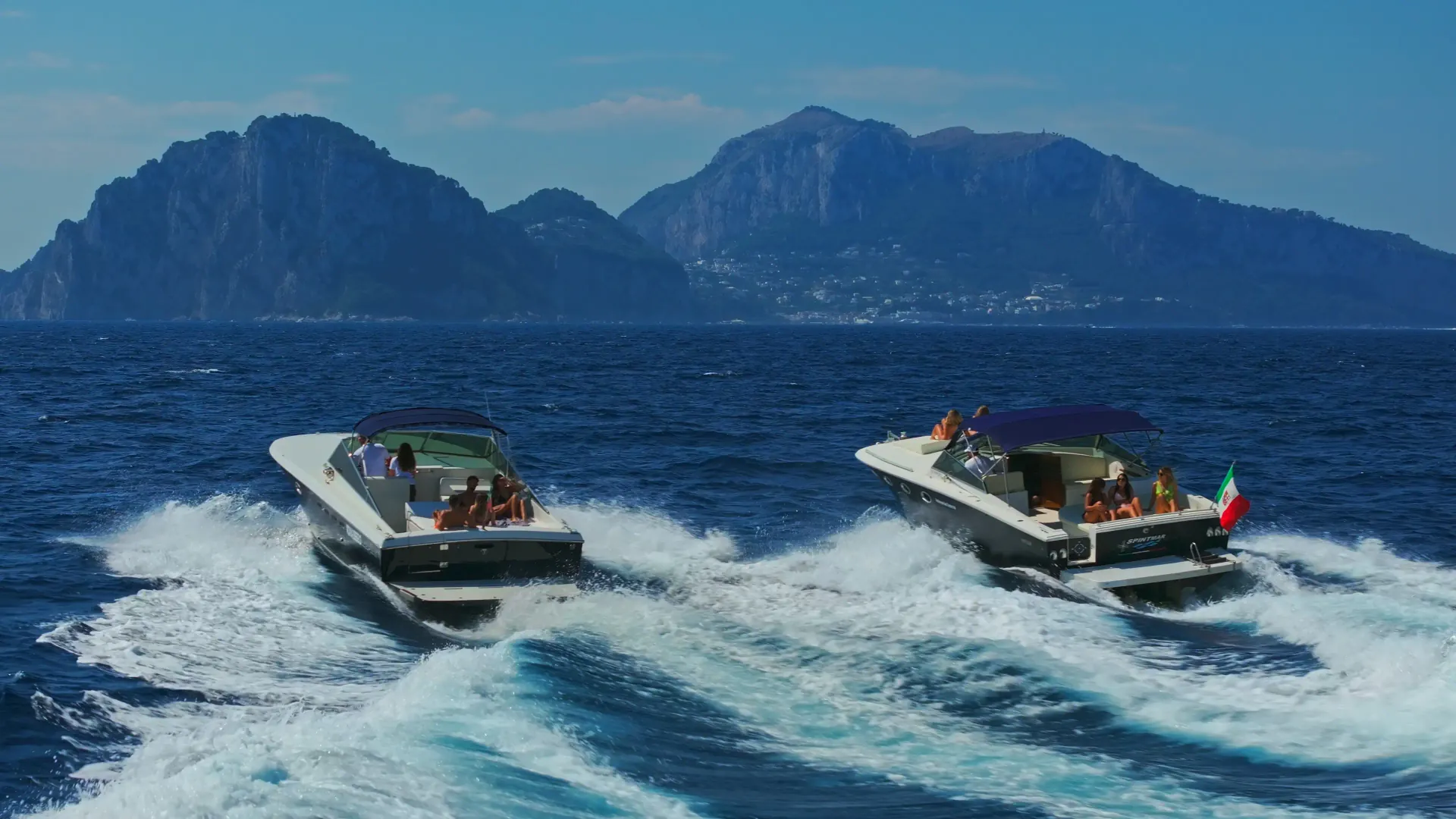 Luxury boat speeding across blue water with Capri mountains